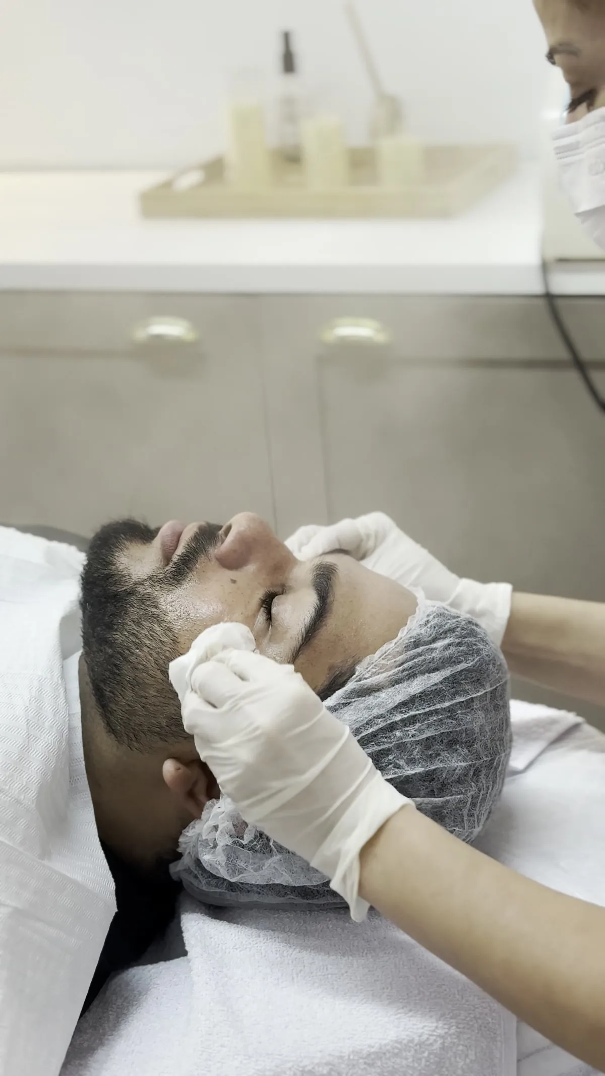Profissional realizando limpeza de pele em um cliente na sala de estética da GÜVEN.